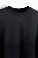 Remera negra de algodón con efecto desteñido, corte cuadrado, cuello redondo ribeteado, hombros caídos y mangas cortas con terminación desflecada.