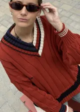 Buzo tejido verde con escote en V, cuello con rayas blancas y azul marino, y puños y ruedo con detalle de rayas.