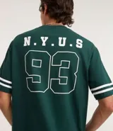 Remera de algodón color verde oscuro, corte relaxed, cuello redondo y manga corta. Presenta un pequeño estampado en el pecho con el texto "N.Y.U.S" en blanco y dos franjas blancas horizontales en cada manga.