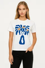 Remera blanca de algodón con estampado de flores azules y naranjas, de corte clásico y cuello redondo.