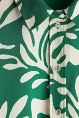 Camisa de manga larga verde con estampado de hojas blancas. Tiene cuello clásico, cierre con botones y puños con botón.