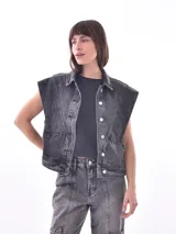 Chaleco de denim azul lavado, sin mangas, con cuello camisero, botones frontales y bolsillos de parche en el pecho.