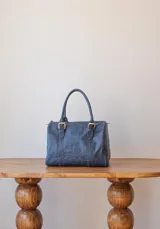 Bolso de mano azul con detalles de costuras verticales y herrajes dorados.