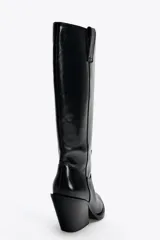 Bota alta de cuero sintético color negro, estilo cowboy, con puntera fina, tiradores laterales y tacón geométrico.