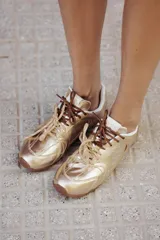 Zapatillas doradas de cuero con cordones marrones y suela marrón.