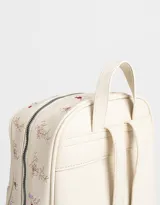 Mochila de cuerina color crema con estampado de flores bordadas, bolsillo frontal con cierre, correas regulables, manija superior, acceso con cierre superior, bolsillos laterales y tag de cuerina.