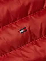 Chaleco acolchado rojo de poliéster reciclado con aislamiento térmico, cuello alto y cierre de cremallera. Tiene dos bolsillos laterales con cremallera, logo de Tommy Hilfiger bordado en el pecho y diseño plegable con acabado repelente al agua.