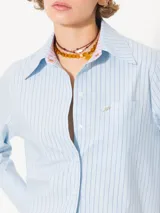 Camisa de poplin rayada rosa y celeste, de corte holgado, con cuello clásico, cierre frontal con botones y bolsillo plaqué en el pecho.