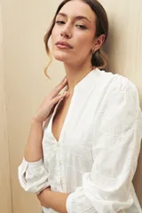 Camisa color beige con bordado floral blanco en toda la superficie. Presenta cuello mao, escote en V y abotonadura frontal, con mangas largas terminadas en puño angosto.