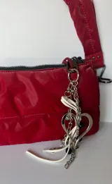 Llavero plateado con dije de corazón irregular, cadenas colgantes con cuentas y cinta de cuero sintético blanca.