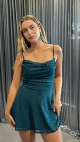Vestido corto de fiesta color verde esmeralda con breteles finos, escote drapeado y falda con vuelo. Tiene pequeños brillos plateados en toda la prenda.