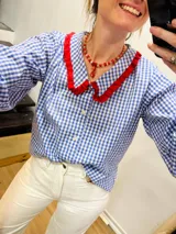 Camisa de algodón a cuadros azules y blancos con cuello y puños con volados rojos.