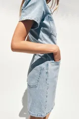Vestido corto de denim azul, con cuello solapa, escote en V, manga corta, bolsillos delanteros y cierre frontal con botones metálicos.