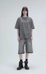 Remera de algodón premium color gris oscuro, corte oversize con hombros caídos y cuello redondo. Estampado grande en la espalda con la palabra "KILOMBITO" sobre una ilustración de una figura en un entorno boscoso en tonos verde azulado y negro.