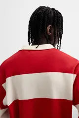Polo de punto con corte relaxed fit, cuello solapa, cierre frontal con botones y manga larga. Diseño a rayas horizontales rojas y blancas.