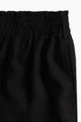 Short negro de corte holgado con tiro alto, cintura elástica fruncida y bolsillos laterales discretos.