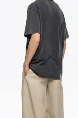 Camiseta de algodón orgánico color beige, corte oversize y manga corta ancha. Presenta un estampado central enmarcado con motivos florales y el texto "BIMBA Y LOLA" en la parte superior e inferior del diseño.