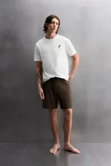 Camiseta blanca de corte holgado confeccionada en tejido de algodón con elasticidad. Tiene cuello redondo, manga corta y estampado en el frente con el logo de la marca y un diseño de tablas de surf.