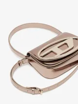Bolso Diesel modelo 1DR, color negro charolado, con asa corta superior y correa bandolera extraíble. Presenta solapa con cierre magnético y logo ovalado "D" metálico en el frente.
