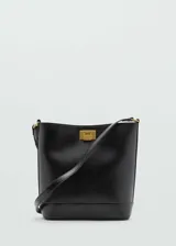 Bolso negro tipo bucket de cuero sintético con correa larga ajustable y extraíble, cierre metálico dorado y asa corta integrada.