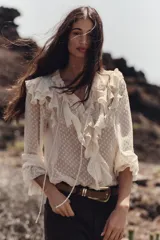 Blusa color crema semitransparente con cuello redondo con volantes y cordón. Manga larga acabada en elástico y volante. Cierre frontal con botones.