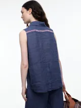 Camisa sin mangas negra de lino con cuello clásico, cierre frontal abotonado y bolsillo de parche en el pecho. Presenta bordados tipo pespunte en contraste en el frente y canesú trasero.