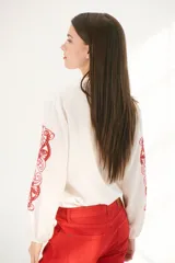 Camisa blanca de manga larga con bordados florales marrones en las mangas.