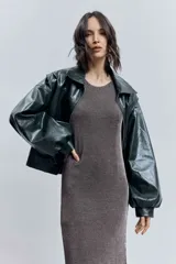 Cazadora corta de efecto piel color verde oscuro, con cuello solapa, cierre frontal de cremallera y mangas largas abullonadas con puños elásticos.