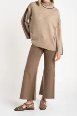 Sweater negro de tejido grueso con cuello alto acanalado. Presenta una franja decorativa en las mangas y el cuello en hilo marrón con brillo (lurex).