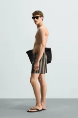 Bañador corto de tejido técnico con rayas verticales en tonos negro, verde oliva y rosa. Cuenta con cintura elástica ajustable con cordón, bolsillos laterales y trasero.