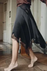 Minifalda negra de satén con corte asimétrico y encaje en el ruedo. Cierre lateral con cremallera oculta.