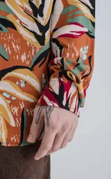 Camisa de manga larga con estampado de flores y hojas en tonos naranja, blanco, rojo, verde y negro.