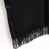 Ruana negra de tejido de punto calado con flecos en el borde inferior.