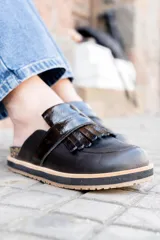 Mocasines negros de cuero con detalle de flecos en la parte delantera y suela gruesa con borde de corcho.