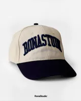 Gorra de béisbol beige con visera y botón superior azul marino. Presenta bordado frontal en azul marino con la inscripción "Bonastun South American League".