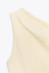 Top de color crema, con escote asimétrico y detalle de pliegues en el hombro.