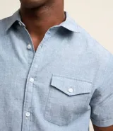 Camisa de hombre de manga corta en lino color blanco, con cuello clásico, botonadura frontal y bolsillo de parche en el pecho. Corte recto.
