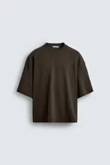 Camiseta marrón de corte amplio, con cuello redondo y mangas cortas. Presenta costuras a la vista en la parte delantera y trasera.