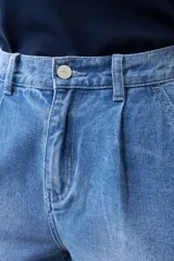 Pantalón de jean celeste de corte ancho, con cintura alta, pinzas y bolsillos laterales. Se ajusta a la cintura con un cinturón de cuero marrón.