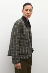 Campera capitoneada con diseño acolchado y estampado a cuadros en tonos verde oliva. Presenta un cuello de pana en color negro, cierre frontal de botones y bolsillos delanteros con ribetes oscuros.