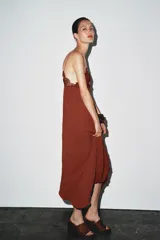 Vestido midi color ladrillo con tirantes finos, escote en pico y detalle de encaje en el busto. Tejido plisado y bajo asimétrico.