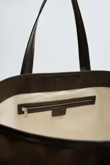 Bolso tipo shopper color marrón, fabricado en tejido de algodón con detalles en piel. Asas fabricadas en piel y algodón. Compartimento principal con cierre mediante imán. El interior cuenta con un bolsillo con cierre mediante cremallera y un bolsillo plano.