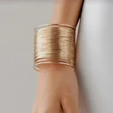 Brazalete rígido dorado, ancho, formado por múltiples aros finos.