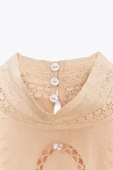 Camisa color crema de algodón con cuello alto, manga larga con puños con volantes y bordados a tono.