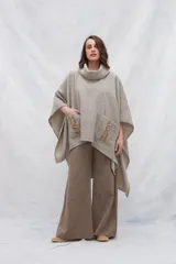 Poncho de lana fina color beige, con cuello alto y bolsillos frontales con detalle de apliques de cuero.