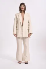 Conjunto de blazer y pantalón de lino color beige. El blazer es de corte recto, con solapas y bolsillos delanteros. El pantalón es de corte palazzo, con cintura alta y pernera ancha.