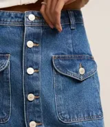 Minifalda de jean azul con bolsillos delanteros con solapa y cierre frontal con botones.