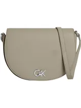 Cartera cruzada Calvin Klein de color beige claro, con forma de media luna o silla de montar. Presenta un logo metálico plateado con las iniciales 'CK' en el frente y una correa ajustable del mismo material.