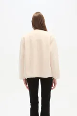 Chaqueta corta de tejido bouclé o pelo sintético color crema, con cuello redondo, cierre frontal metálico y dos bolsillos frontales amplios.