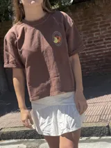 Remera color chocolate con cuello redondo y mangas cortas con dobladillo. Estampado circular en el pecho con dibujo de frutas y texto.